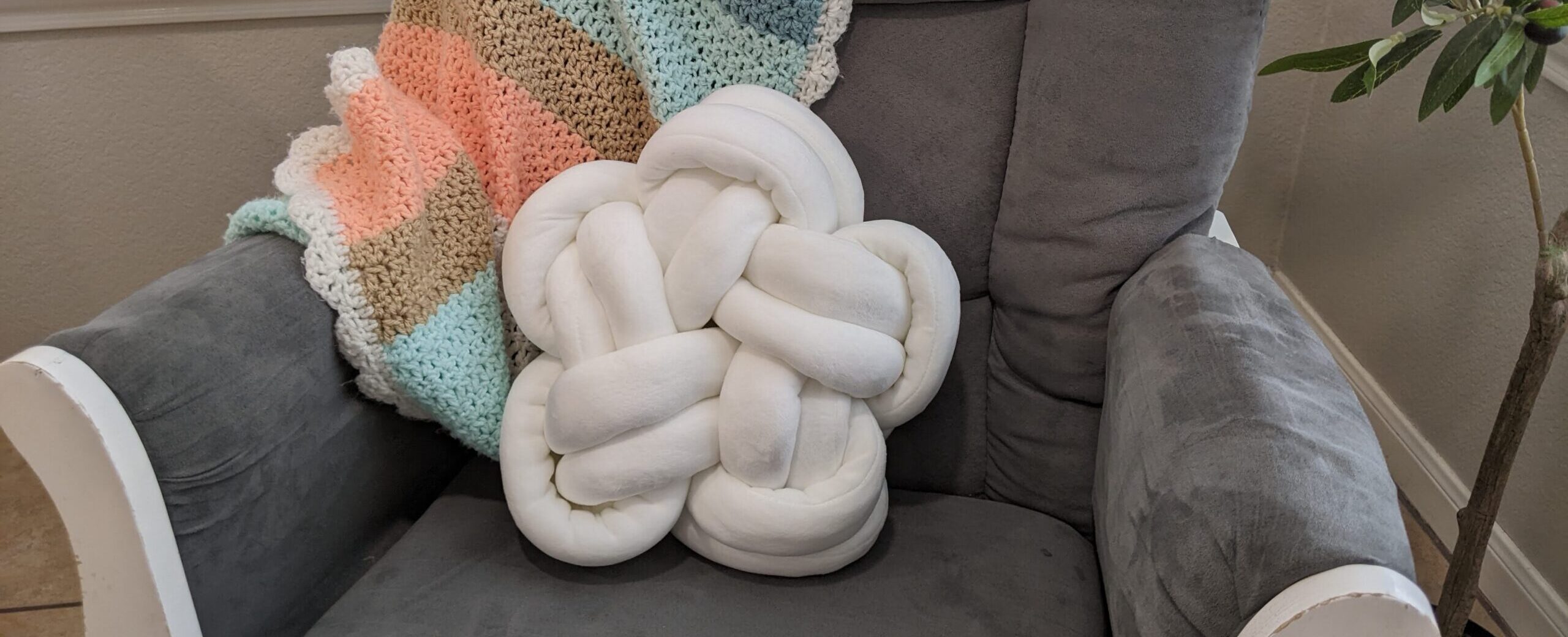 White star-shaped knot pillow on a gray armchair with a cozy crocheted blanket