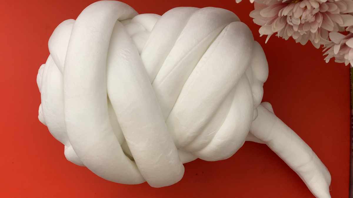 Close-up of a white knot pillow ball made from jumbo tube yarn on a red background
